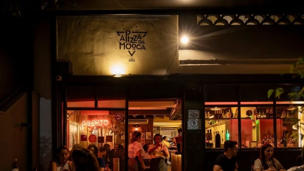Entrada Iluminada Da Pizzaria A Pizza Da Mooca Com Clientes Na Calçada E Ambiente Interno Visível