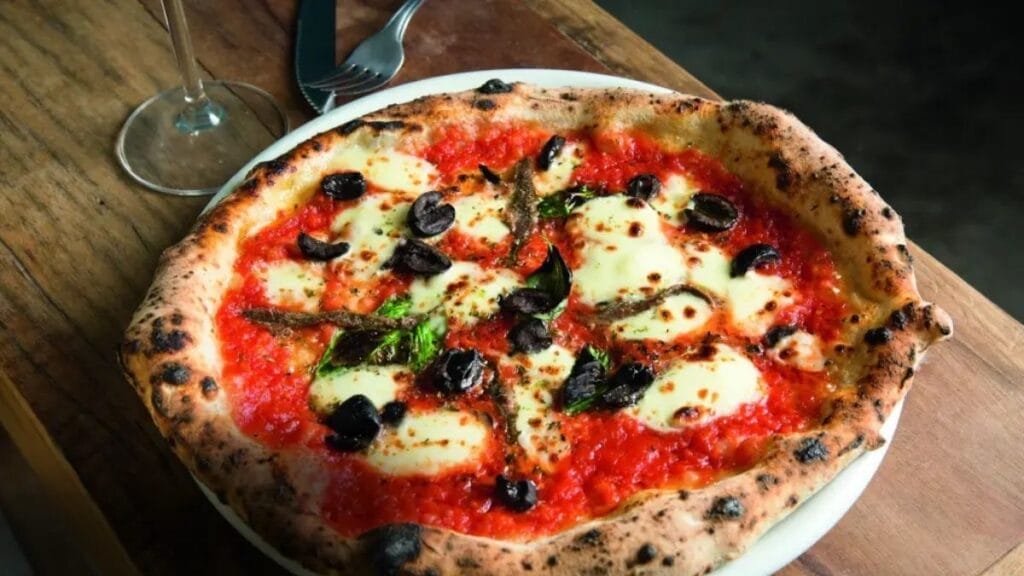 Pizza Napolitana Da Leggera Com Borda Alta, Molho De Tomate, Mussarela, Azeitonas E Aliche Sobre Mesa Rústica